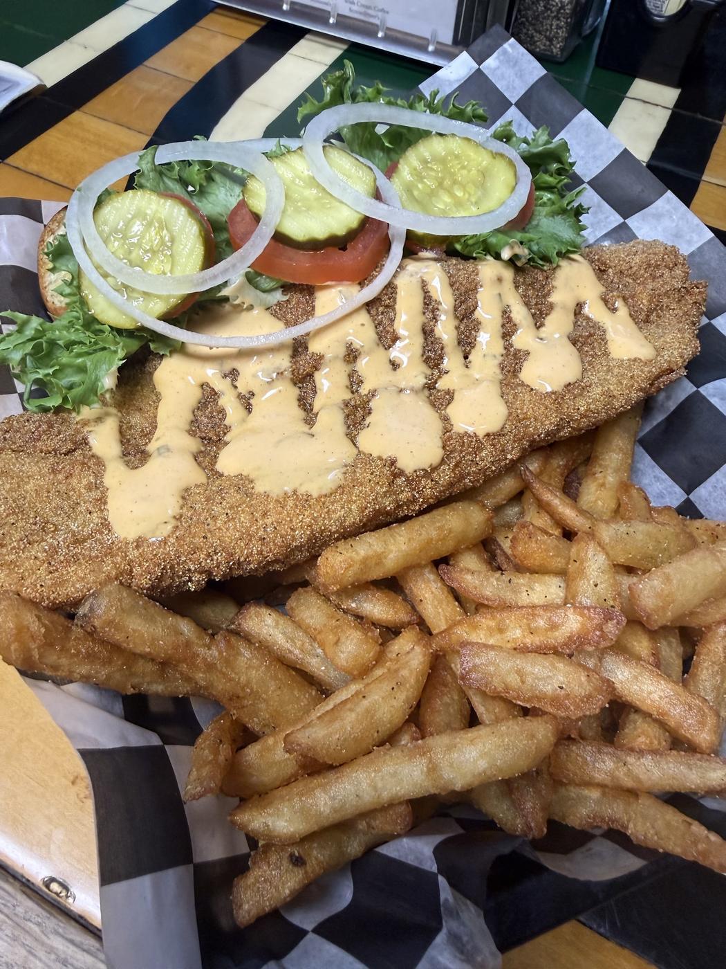 A breaded catfish fillet with sauce and a basket of seasoned fries