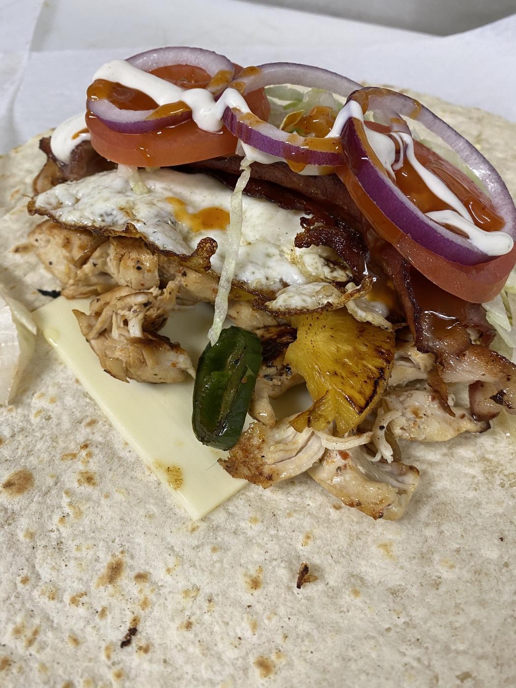 An open faced grilled chicken sandwich with a fried egg, pineapple, tomato and red onion