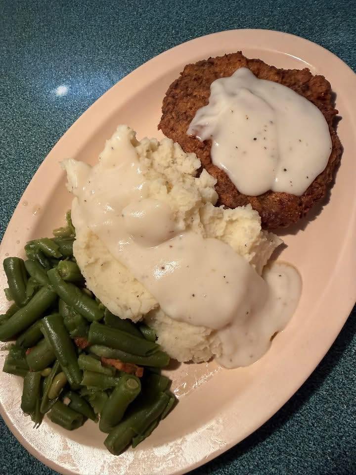Country fried steak under white gravy with mashed potatoes and green beans