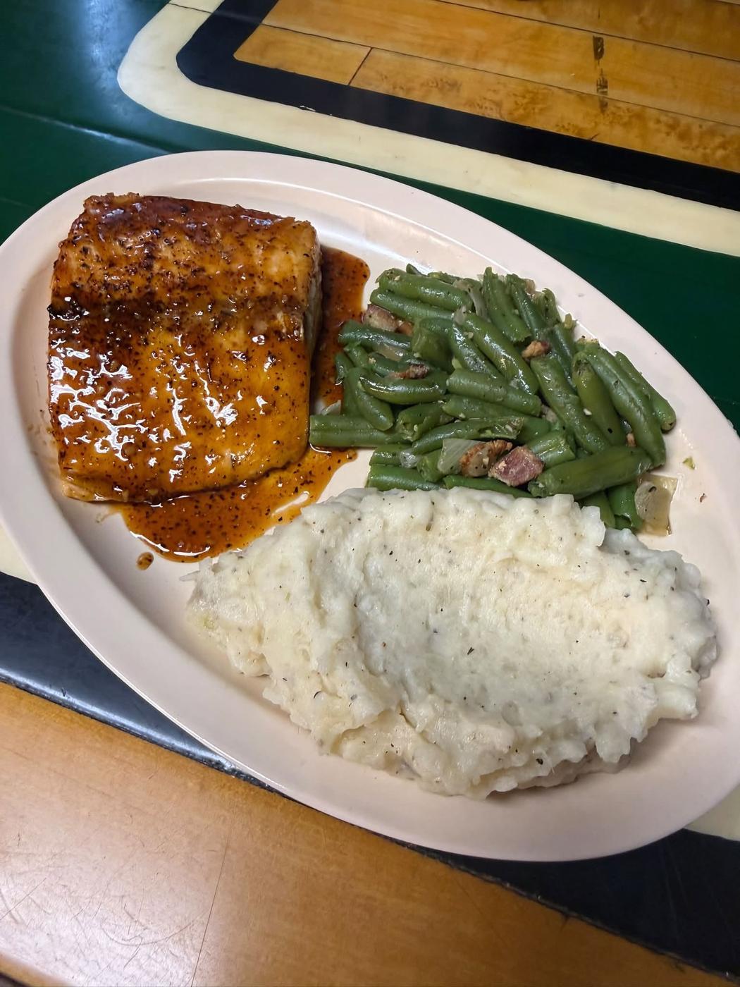 A glazed salmon fillet with green beans and mashed potatoes on an oval plate