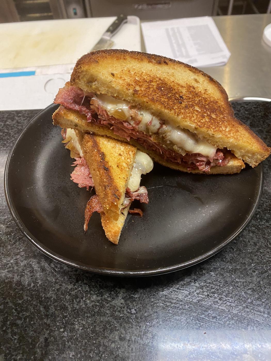 A grilled sandwich cut in half on a dark plate, showing the meat and melted cheese