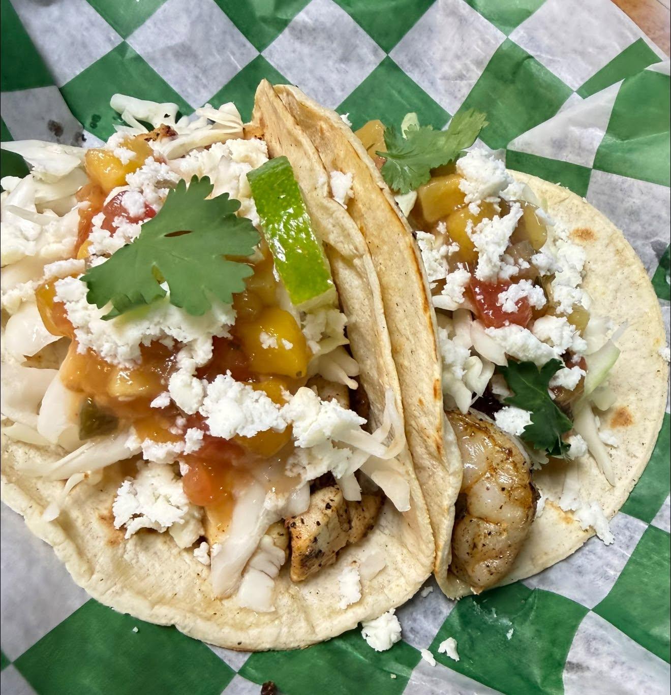 Two soft tacos with grilled chicken and shrimp, cotija, cabbage, cilantro and a wedge of lime