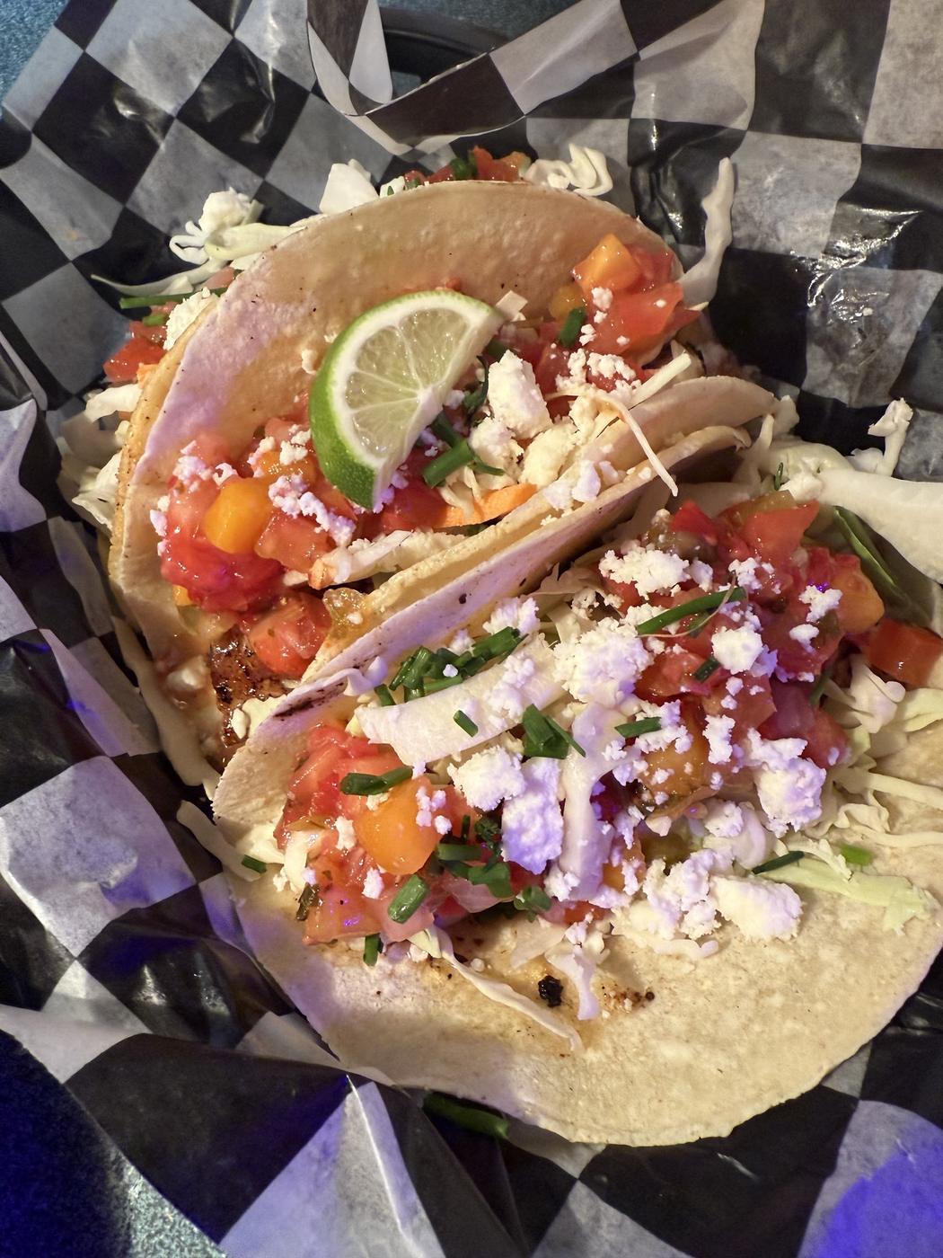Two tacos loaded with pico de gallo and crumbled cotija, with lime
